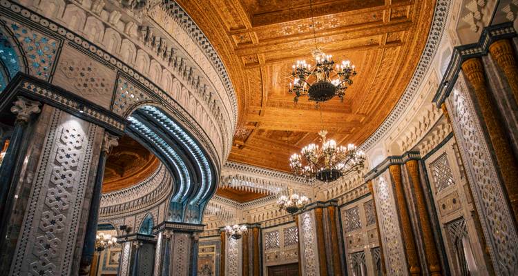 Salle intérieure somptueusement décorée avec plafond en bois sculpté, lustres et murs aux motifs complexes.