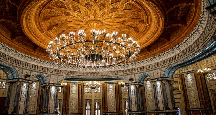 Grand hall circulaire au plafond orné d'une rosace en bois sculptée et d'un lustre éclatant, entouré de murs en mosaïque.