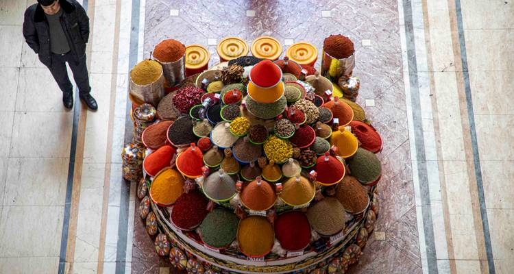 Présentation pyramidale colorée d'épices et de céréales dans un marché couvert avec un client debout à proximité.