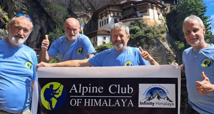 Four men in matching shirts hold a promotional banner with the cliffside monastery behind them.