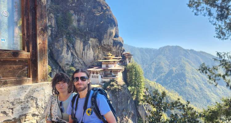 Couple with backpacks posing near a window overlooking Bhutan's famed cliff monastery.