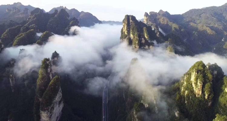 Vue aérienne de hauts piliers de grès s'élevant au-dessus d'une mer de nuages ondulants dans un paysage montagneux spectaculaire.