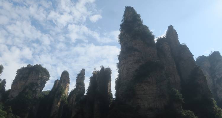 Des tours de grès déchiquetées avec des parcelles de verdure s'élèvent dans un ciel bleu parsemé de petits nuages.
