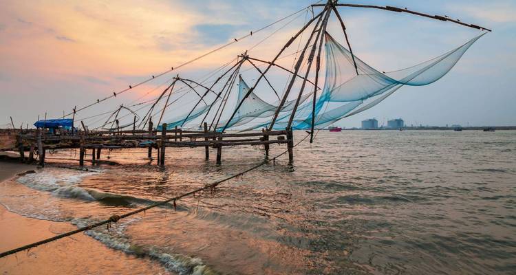 D'iconiques filets de pêche chinois s'étendent au-dessus de la mer d'Arabie au coucher du soleil, les vagues léchant le rivage sablonneux.