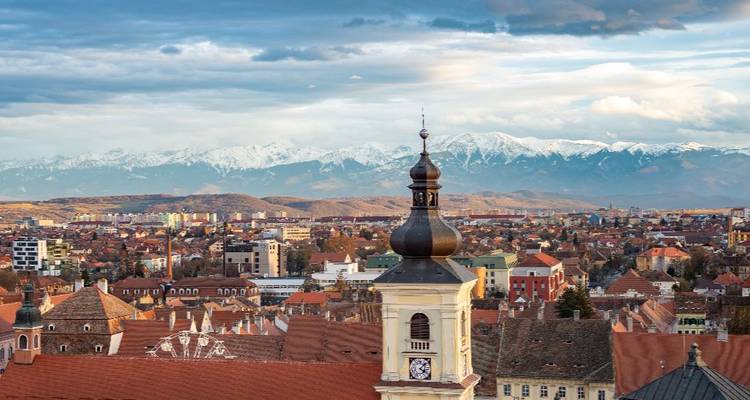 Panoramisch uitzicht over de daken van Sibiu met kerktoren en besneeuwde Făgăraș-bergen in de verte