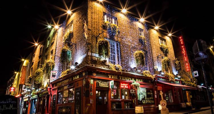 Iconic Temple Bar pub glows with lights and hanging plants on a lively cobbled street at night.