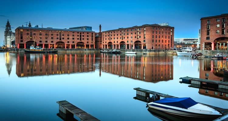 Historic brick warehouses of Liverpool's Albert Dock beautifully mirrored in still morning water with small boats.