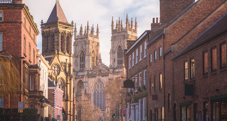 Historic street scene framing the towering Gothic façade of York Minster between brick and stone townhouses.