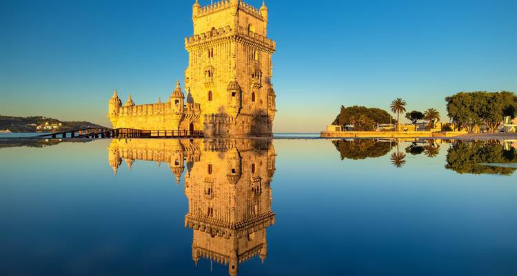 Torre de Belém y su reflejo perfecto como espejo en aguas tranquilas bajo la cálida luz dorada del amanecer.