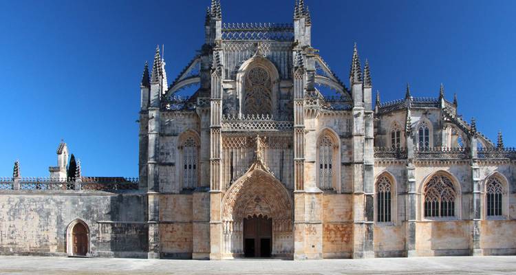 Impresionante fachada de monasterio gótico con intrincada cantería bajo un cielo azul profundo.