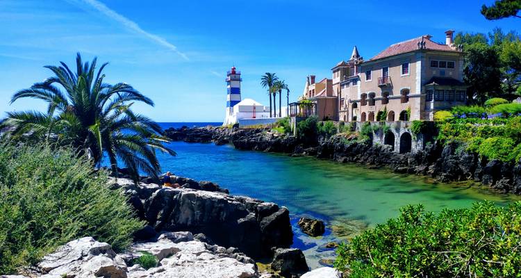 Cala pintoresca con agua turquesa, palmeras y un faro junto a elegantes villas costeras.