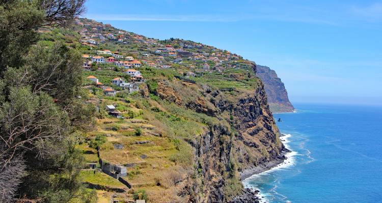 Las casas del pueblo en terrazas se aferran a los espectaculares acantilados marinos de Madeira sobre el profundo Atlántico azul.