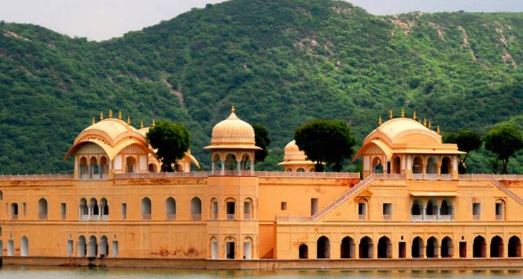 Blassgelbder Jal Mahal Wasserpalast vor üppigen grünen Hügeln