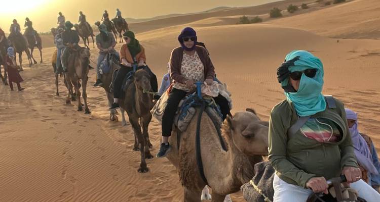 Kameelkaravaan die reizigers draagt over gouden duinen bij zonsondergang.