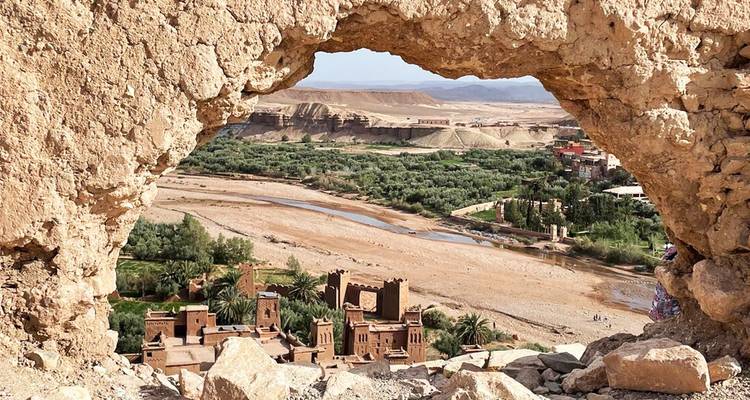 Zicht op de kasbah van Ait Benhaddou door een natuurlijke rotsvenster hoog boven de vallei.