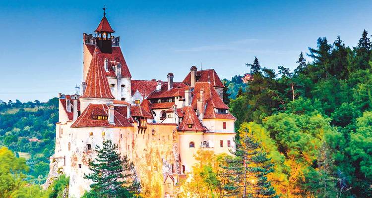 Het sprookjesachtige Kasteel Bran rijst uit boven het groene bos onder een helderblauwe hemel in Roemenië.