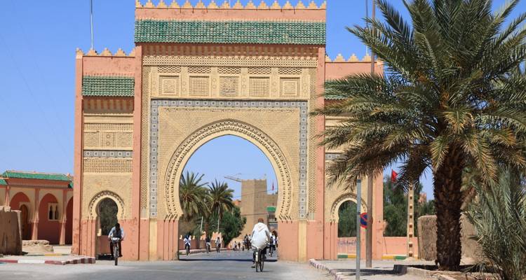 Grand decorative desert gateway with motorcyclists passing beneath against a clear blue sky.