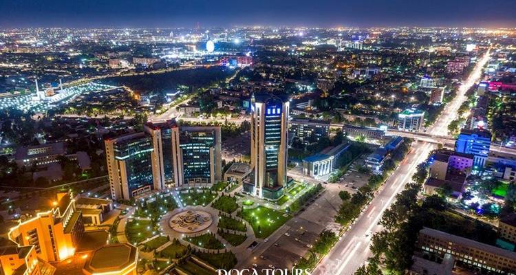 Panorama aérien nocturne d'une ville moderne vivement éclairée avec des immeubles de grande hauteur, de longues avenues et des lampadaires lumineux.