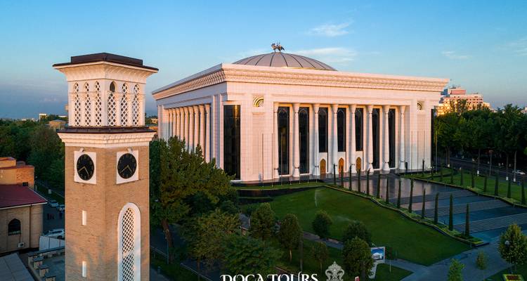 Élégant hall néoclassique blanc avec de hautes colonnes à côté d'une tour d'horloge historique en brique à l'heure dorée.