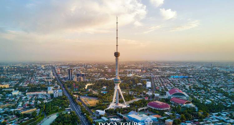 Vue aérienne en plongée d'une ville étalée dominée par une haute tour de télévision s'élevant au-dessus des toits sous la lumière du coucher de soleil.