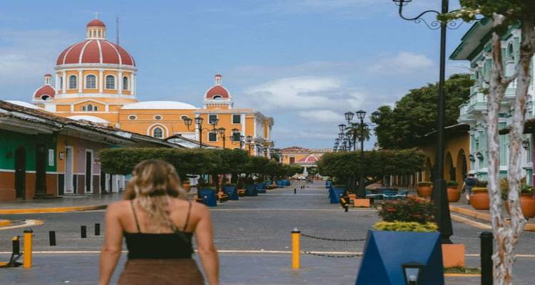 Jeune femme marche dans une rue coloniale colorée vers le dôme rouge de la cathédrale de Grenade.