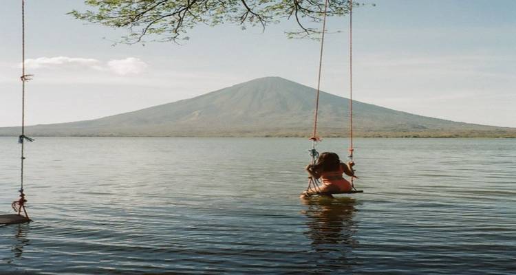 Voyageur sur balançoire au-dessus du lac avec volcan conique s'élevant en arrière-plan sur l'île d'Ometepe.
