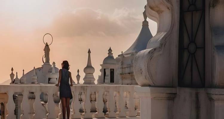 Un visiteur contemple les dômes blancs ornés et les flèches de la toiture de la cathédrale de León au coucher de soleil pastel.