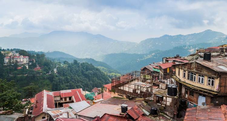 Dachblick über die farbenfrohe Hügelstadt Shimla mit nebligen Bergen im Hintergrund.