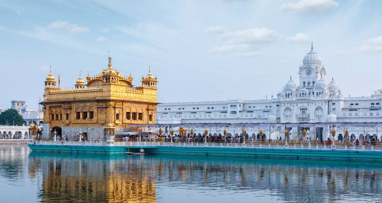 Der Goldene Tempel schimmert neben seinem spiegelglatten heiligen Teich, während Gläubige über den marmornen Damm wandeln