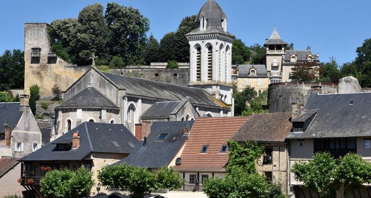 Close-up zicht op een kerkcomplex op een heuveltop en historische stenen gebouwen onder heldere blauwe luchten in landelijk Frankrijk.
