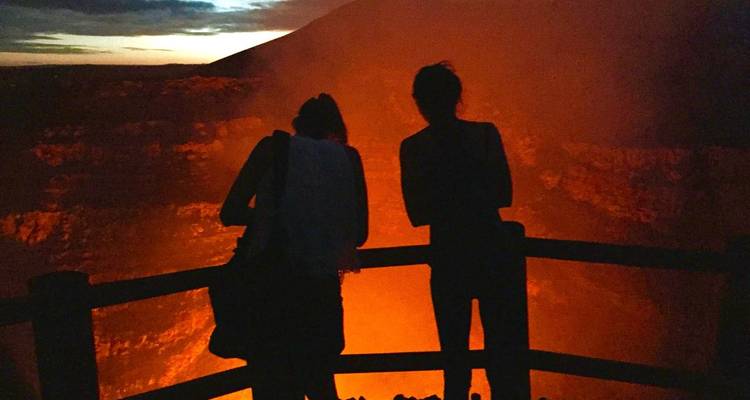 Visitantes en silueta observan un cráter volcánico resplandeciente al anochecer.