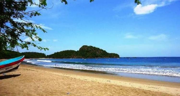 Una playa de arena tranquila se encuentra con un mar azul calmado bajo un cielo despejado, con un barco colorido a un lado.
