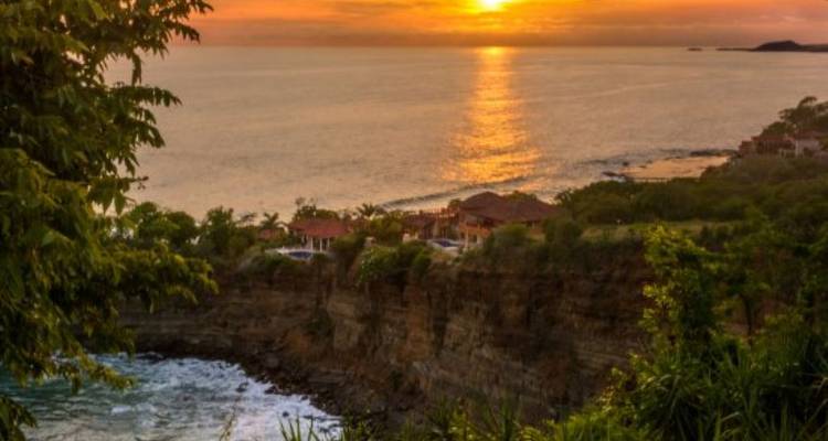 Un sol dorado se pone sobre el océano, su reflejo brillando junto al borde de un acantilado rocoso.