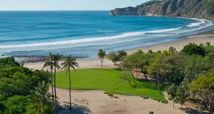 Las palmeras enmarcan un green de golf junto a la playa al lado de las ondulantes olas del Pacífico.