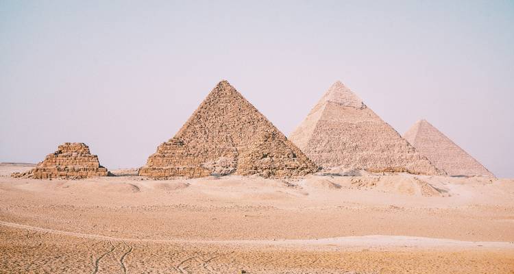 Die ikonischen Pyramiden von Gizeh ragen scharf aus dem goldenen Sand der Sahara unter einem blassen blauen Himmel empor.