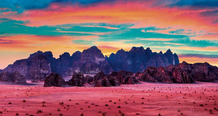 Dramatische rot getönte Wüstenlandschaft mit zerklüfteten Felsformationen, die sich gegen einen lebendigen, mehrfarbigen Sonnenuntergangshimmel abzeichnen.