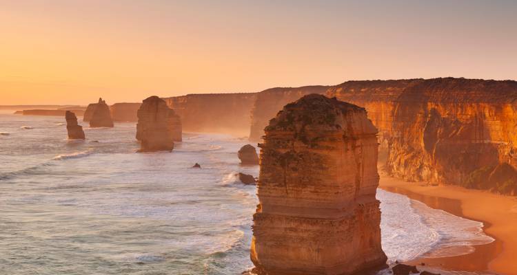 Lueur dorée sur les hautes cheminées de mer calcaires et les falaises le long d'un littoral océanique accidenté.