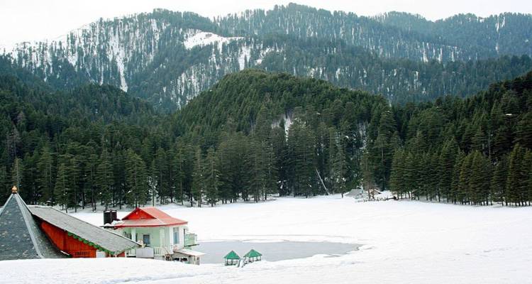 Schneebedeckte Wiese mit einem zugefrorenen See, umgeben von dichten Kiefernwäldern und umliegenden Hügeln.