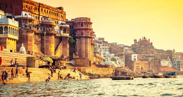 Historic riverfront palaces and stone steps of Varanasi glow under golden evening light as boats dot the Ganges.