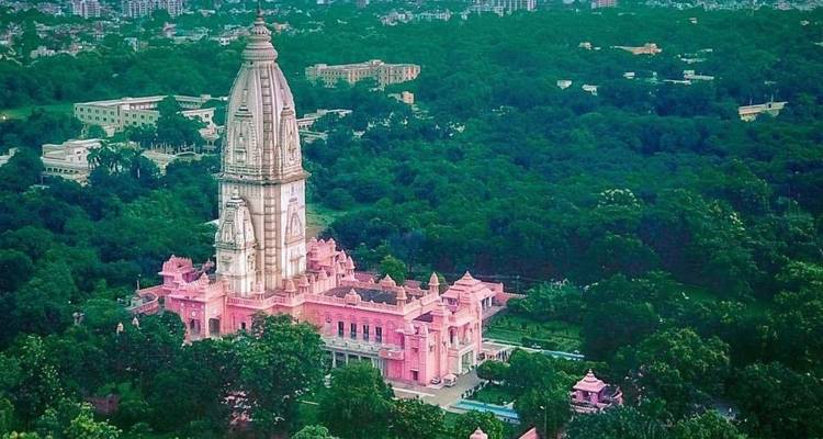 Aerial view of tall pink sandstone temple surrounded by lush green forest canopy.