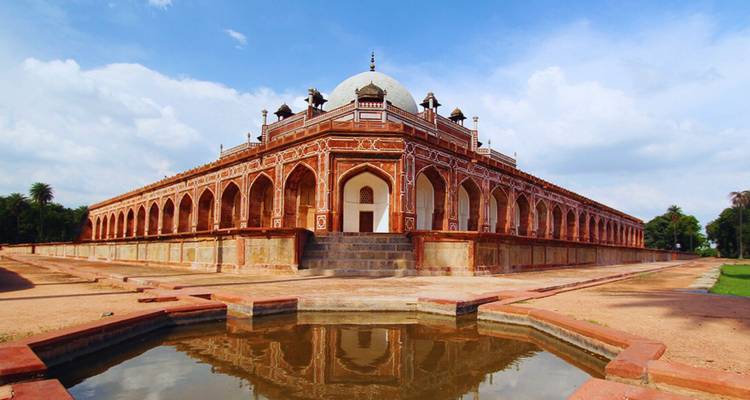The symmetrical red-sandstone and marble Humayun’s Tomb reflects elegantly in a small pool under a blue sky.