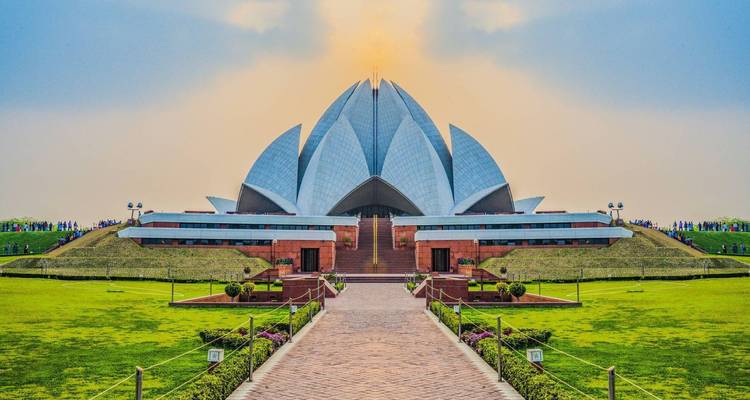 The iconic Lotus Temple with its petal-shaped marble shells sits amid lush gardens under a warm dusky sky.