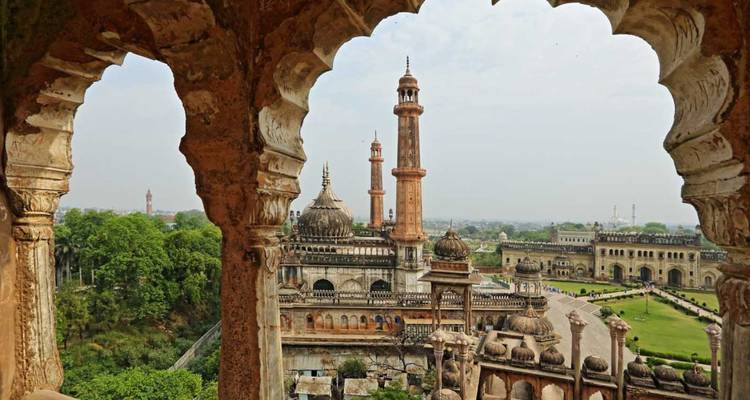 An ornate sandstone arch frames the sprawling Bara Imambara complex with minarets rising above green gardens.