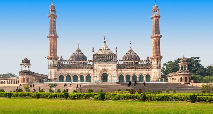 Front view of Lucknow’s Bara Imambara with twin minarets and manicured lawns beneath a bright blue sky.