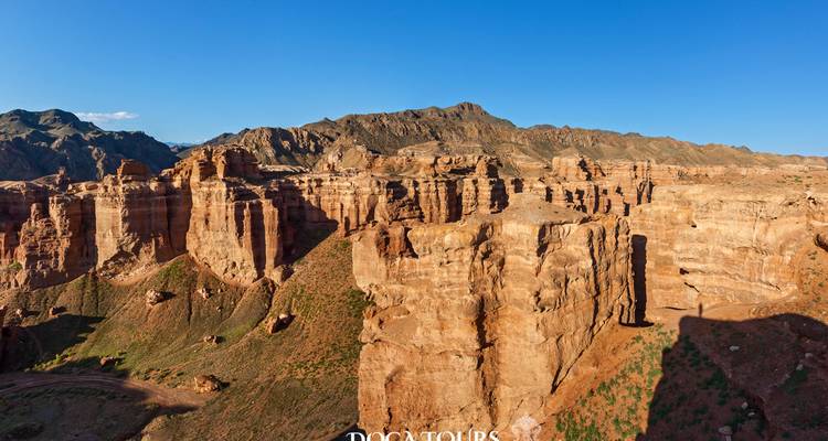 Falaises et pinacles de grès rougeâtre d'un paysage de canyon avec un filigrane de logo visible.