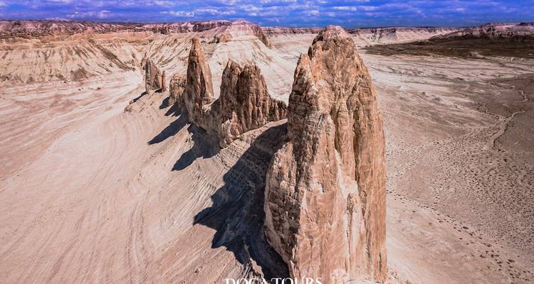 Vue aérienne de formations rocheuses spectaculaires et déchiquetées s'élevant d'une vaste plaine désertique aride sous un ciel bleu.