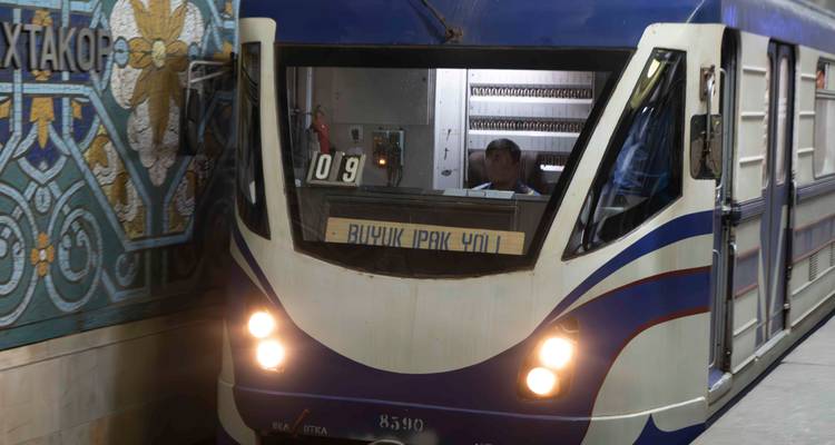 Train de métro bleu et blanc entrant dans une station souterraine aux carreaux ornementés.