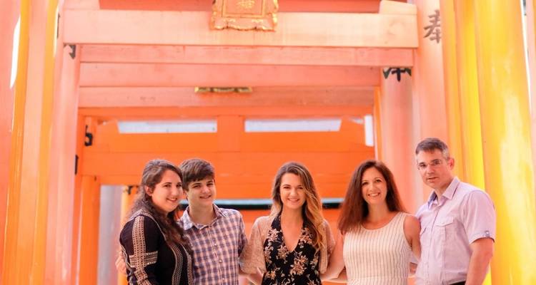 Family poses beneath bright orange torii gates of Fushimi Inari shrine.