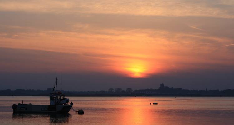 Petit bateau ancré sur une eau calme pendant un coucher de soleil orange vif