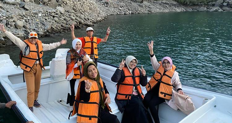 Un groupe joyeux portant des gilets de sauvetage orange pose dans un bateau à moteur blanc sur un lac vert profond entouré de rives rocheuses.